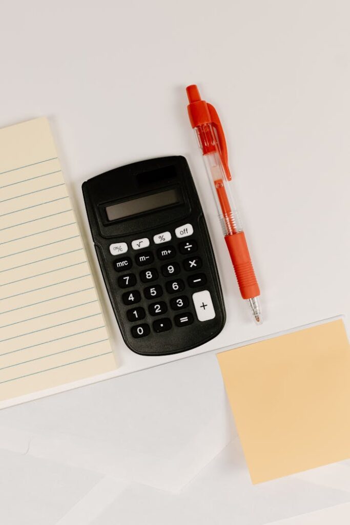 Black calculator, red pen, and paper on a white surface with ample copy space.