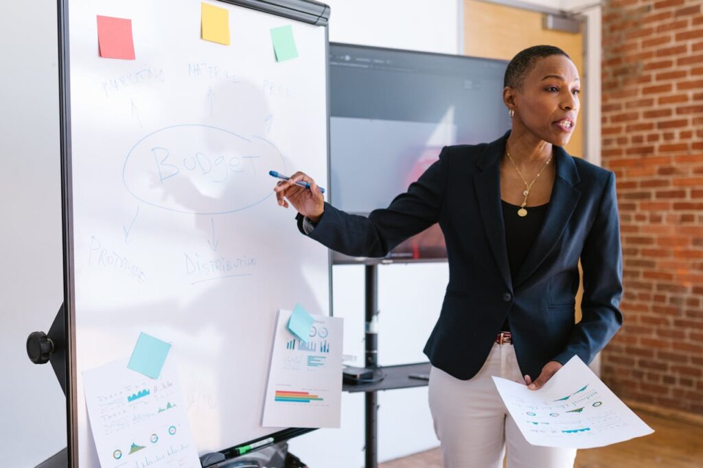 Professional businesswoman explaining budget strategy on a whiteboard during a meeting.